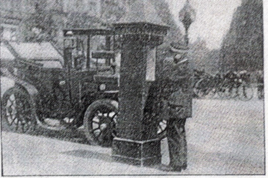 Ausschnitt derselben Aufnahme: die gemauerte Rufsäule am Straßenrand, ein Mann in Uniform am Hörer, dahinter eine offene Motordroschke am Halteplatz.